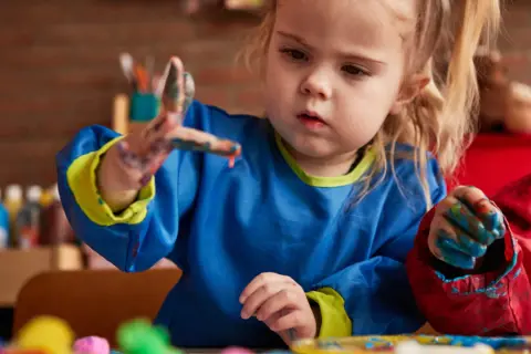 Een peuter met verf aan haar handen, die geconcentreerd aan het schilderen is. Dit is een mooi voorbeeld van cognitieve ontwikkeling peuter door creatief spel.