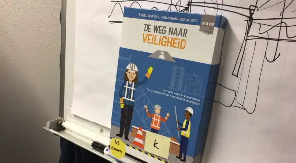 Doos van het spel "De Weg Naar Veiligheid" met bouwfiguren. Het spel moedigt aan om nog veiliger te werken, zodat iedereen veilig gespeld wordt.