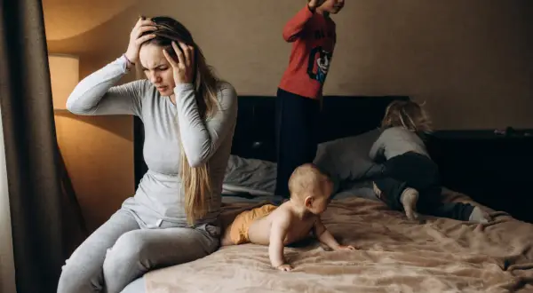 Een moeder met handen in haar hoofd, overdonderd door de drukte van haar kinderen. Een dag met adhd en autisme kan intens zijn.