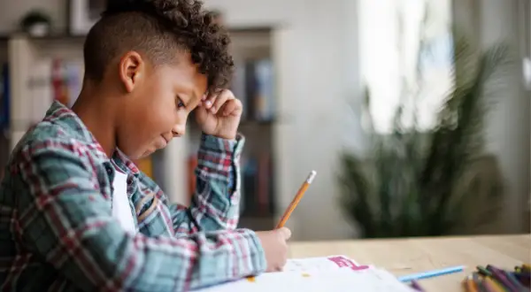 Jongen met krullend haar verdiept in zijn huiswerk, een potlood in zijn hand, navigeert door de wereld van getallen.