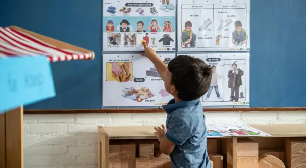 Jongen wijst naar een poster met kledingstukken en geld, onderdeel van woordenschat groep 4.