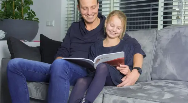 Vader en dochter lezen samen een rekenboek. De tafels flitsen door hun hoofd terwijl ze oefenen.