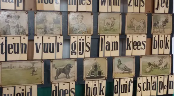 Oude letterkaarten met afbeeldingen, die samen Nederlandse uitdrukkingen vormen zoals 'aap, noot, mies'.