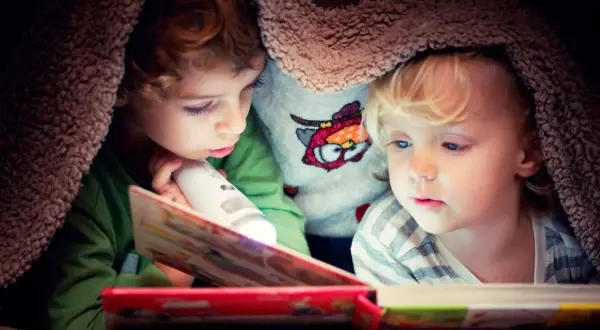 Twee kinderen lezen onder een deken met een zaklamp. Een verhaal dat de woordenschat van groep 8 verrijkt.
