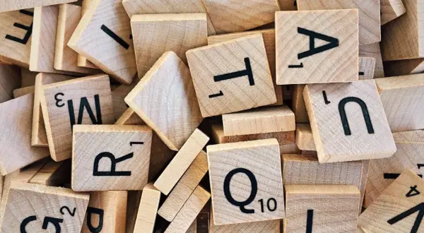 Houten lettertegels, zoals gebruikt bij moderne vreemde talen, liggen door elkaar. Letters als A, T, R, Q en N zijn zichtbaar.