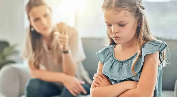 Een meisje met gekruiste armen toont duidelijk oppositioneel gedrag, terwijl haar moeder op de achtergrond met haar vinger waarschuwt.
