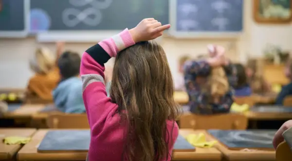 Een meisje met dyscalculie op de middelbare school steekt haar vinger op, hopend op hulp bij de sommen op het bord.