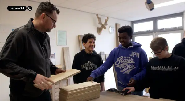 Docent toont hout aan leerlingen. Een van hen, met een blauwe hoodie, lacht. Dit is een cluster 4 indicatie voor praktijkonderwijs.