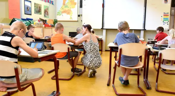 Een lerares geeft individuele aandacht aan leerlingen in een klaslokaal, wat de kern vormt van traumasensitief onderwijs.