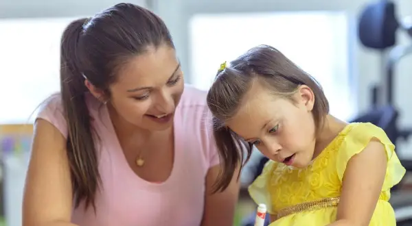Een vrouw helpt een meisje met autisme met haar huiswerk. Ze probeert haar zin te doordrijven en te motiveren.
