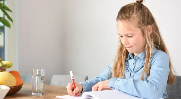 Een meisje schrijft in haar schrift, geconcentreerd op het oplossen van ongelijknamige breuken. Een glas water en fruit staan klaar.