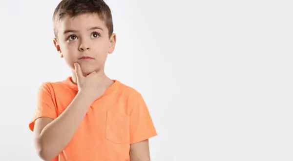 Jongetje met oranje shirt denkt diep na, misschien een beetje traag van begrip, met zijn vinger op zijn kin.