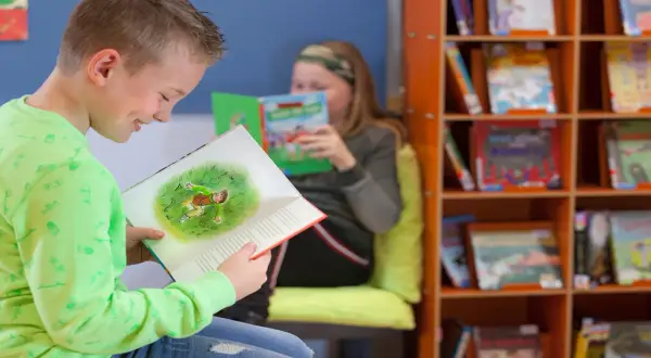 Jongen in groen shirt geniet van een boek met een illustratie. Achter hem leest een meisje. Dit is een typisch beeld van lezen groep 4.