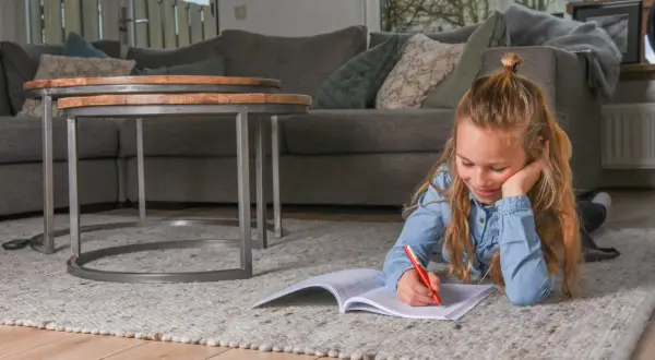 Een meisje ligt op een kleed en maakt huiswerk, ze oefent met breuken delen.