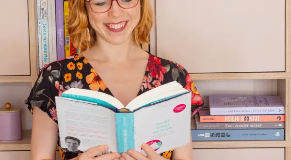 Vrouw met bril leest boek, "nooit meer te druk". Ze is omringd door boeken, wat een **betrekkelijk voornaamwoord** is voor haar passie.
