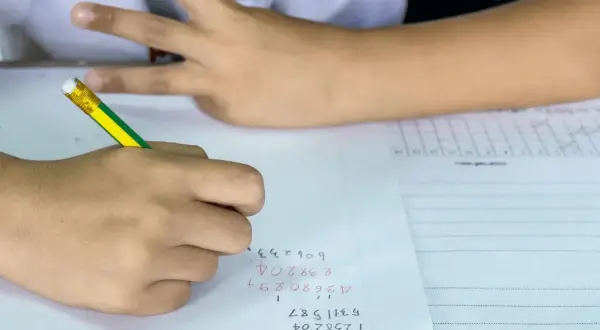 Een leerling uit groep 8 is bezig met rekenen. De leerling schrijft cijfers op papier, met een potlood.