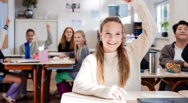 Vrolijke leerlingen steken hun hand op in een klaslokaal. De sfeer is positief, ondanks de mogelijke particulier onderwijs kosten.