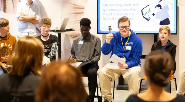Jongeren presenteren hun bevindingen over de geschillencommissie passend onderwijs. Een jongen met een trofee lacht naar de camera.