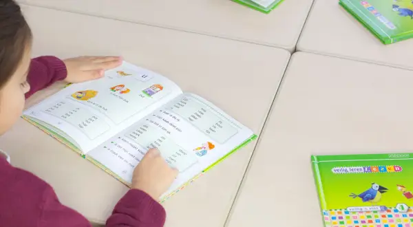 Meisje leest in een boek om technisch lezen te verbeteren. Woorden en zinnen helpen haar met oefenen.