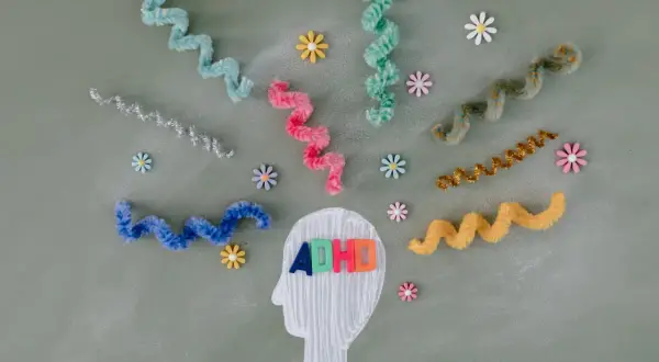 Kleurrijke linten en bloemen omringen een hoofdprofiel met de letters "ADHD". Dit symboliseert de zoektocht naar een kind behandeling.