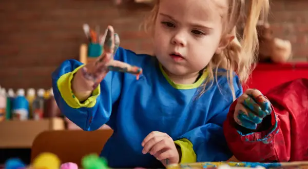 Een peuter met verf aan haar handen, die geconcentreerd aan het schilderen is. Dit is een mooi voorbeeld van cognitieve ontwikkeling peuter door creatief spel.