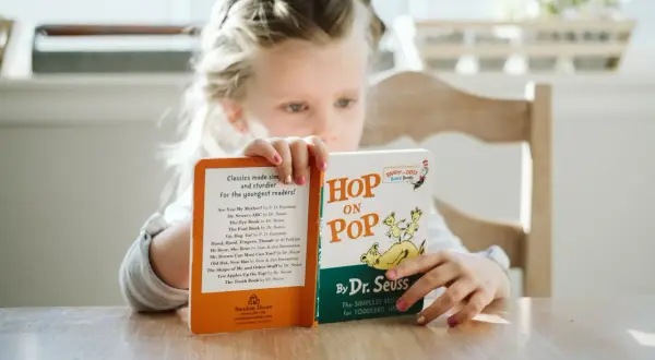 Een meisje van avi m4 leeftijd leest met plezier "Hop on Pop" van Dr. Seuss.
