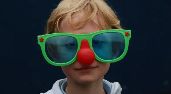 Kind met clownesk gedrag, autisme. Grote groene bril met rode neus, blauwe glazen.