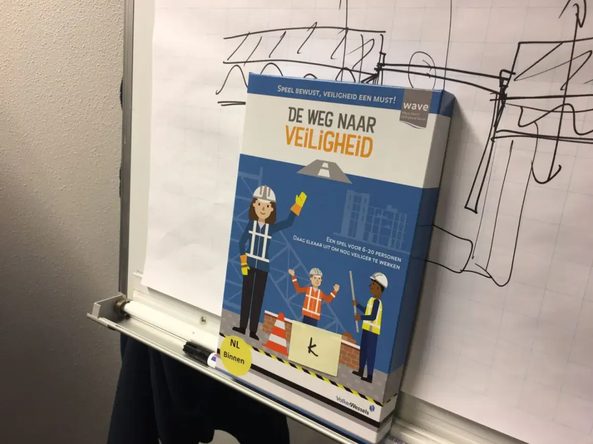 Doos van het spel "De Weg Naar Veiligheid" met bouwfiguren. Het spel moedigt aan om nog veiliger te werken, zodat iedereen veilig gespeld wordt.