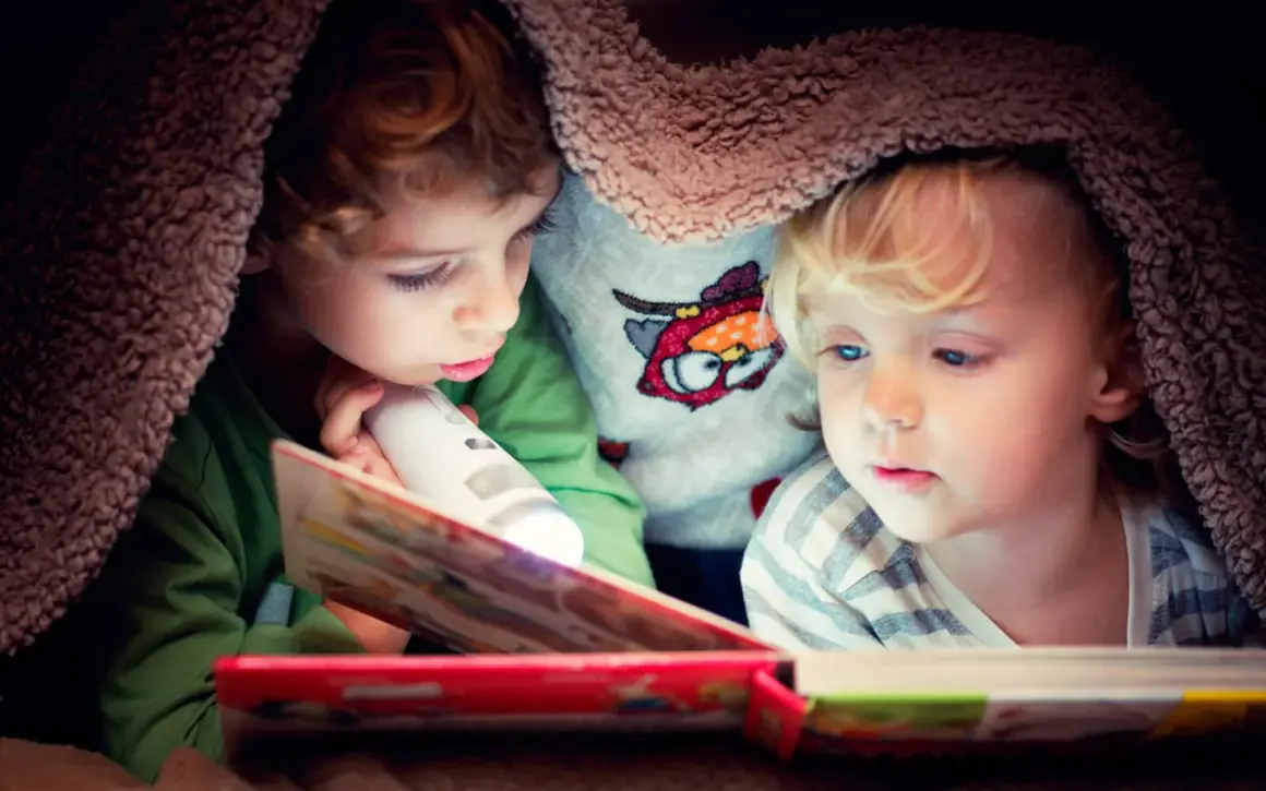 Twee kinderen lezen onder een deken met een zaklamp. Een verhaal dat de woordenschat van groep 8 verrijkt.
