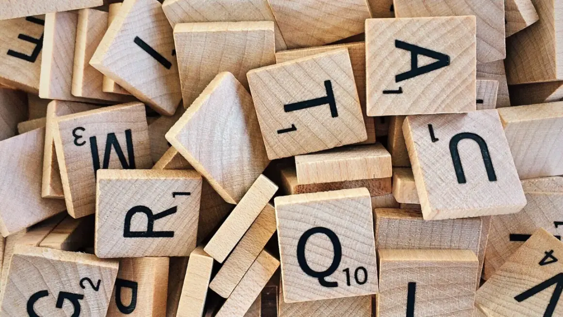 Houten lettertegels, zoals gebruikt bij moderne vreemde talen, liggen door elkaar. Letters als A, T, R, Q en N zijn zichtbaar.