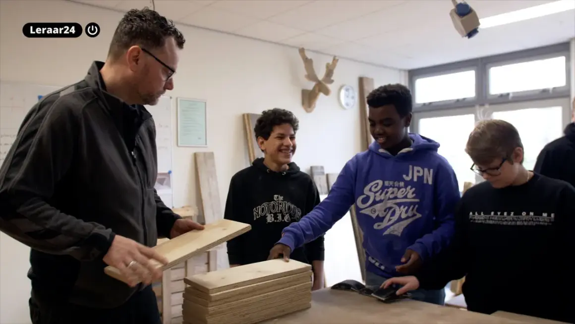 Docent toont hout aan leerlingen. Een van hen, met een blauwe hoodie, lacht. Dit is een cluster 4 indicatie voor praktijkonderwijs.