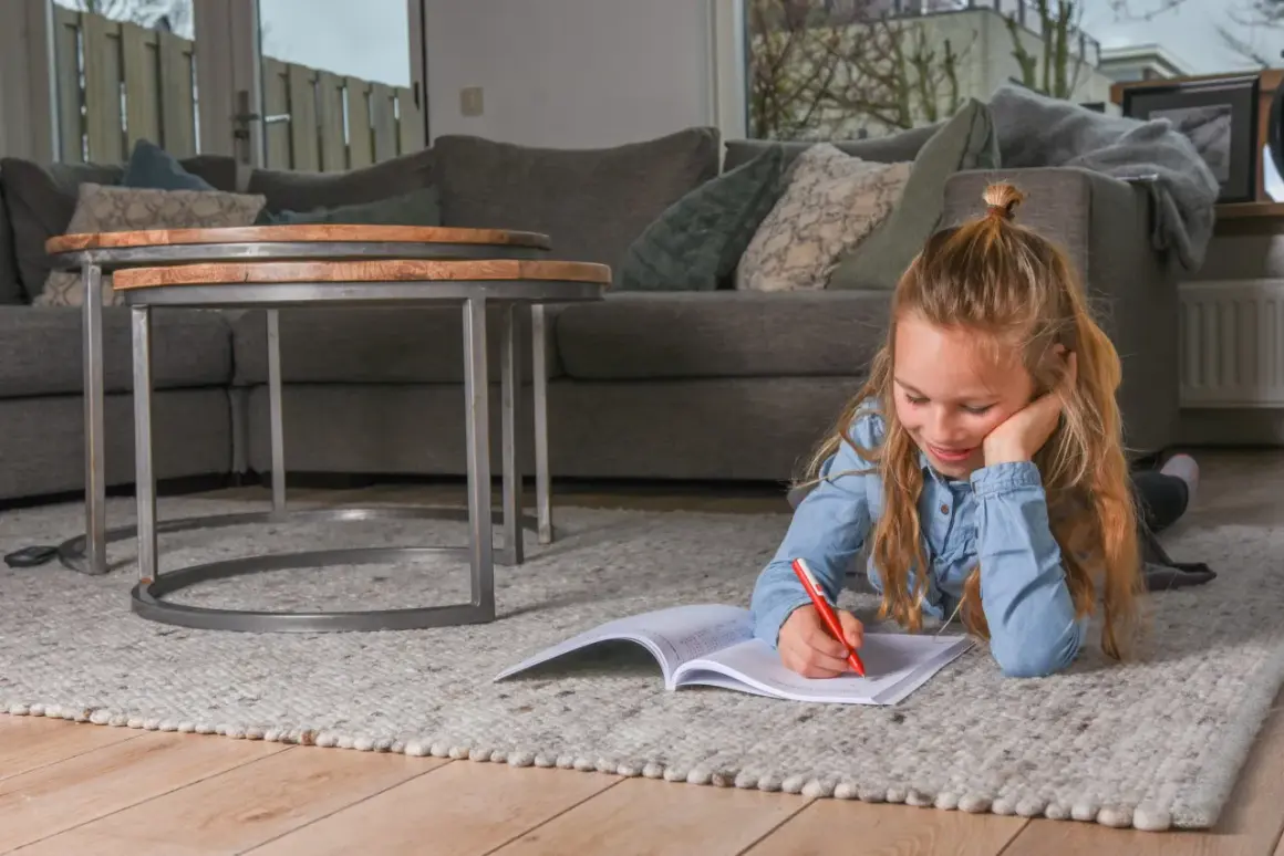 Een meisje ligt op een kleed en maakt huiswerk, ze oefent met breuken delen.