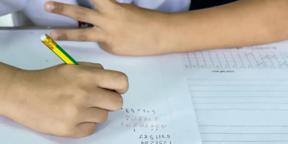 Een leerling uit groep 8 is bezig met rekenen. De leerling schrijft cijfers op papier, met een potlood.