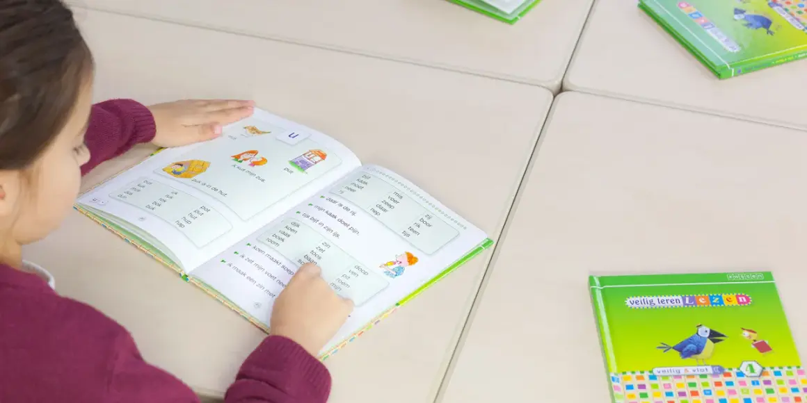 Meisje leest in een boek om technisch lezen te verbeteren. Woorden en zinnen helpen haar met oefenen.