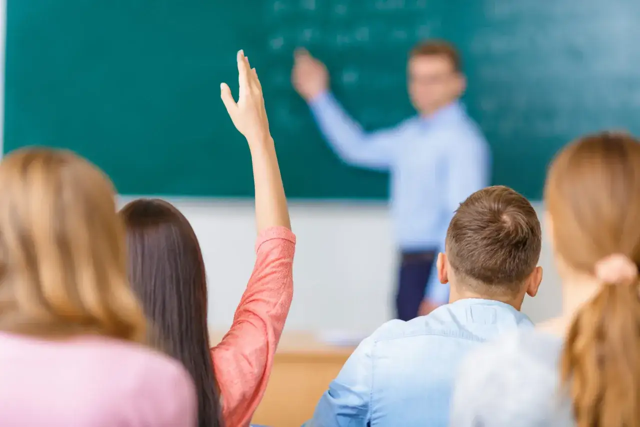 Leerlingen met opgestoken handen in een klaslokaal, klaar om vragen te beantwoorden. Dit toont interactief onderwijs.
