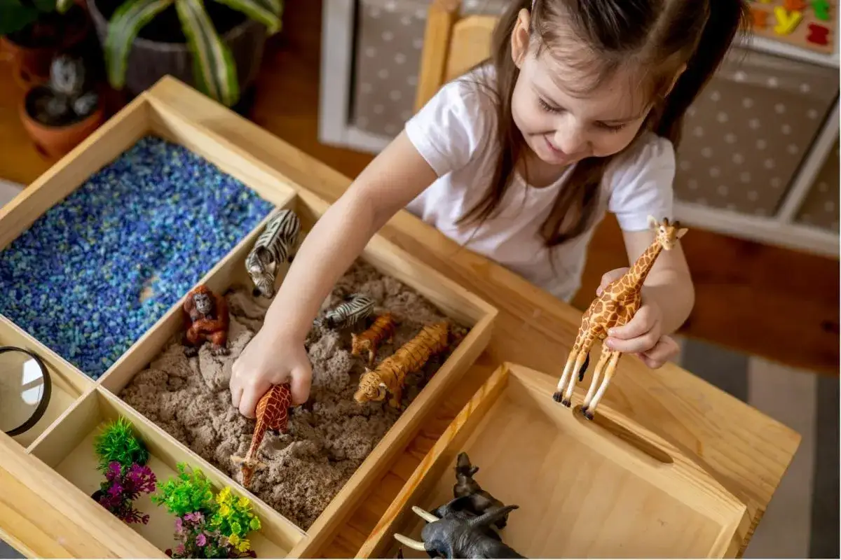 Meisje speelt met dierenfiguren in een zandbak, wat de cognitieve ontwikkeling van een peuter stimuleert. Ze ontdekt de wereld.