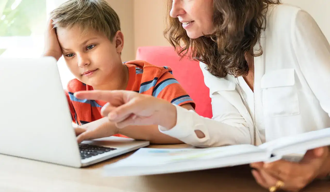 Jongen leert moderne vreemde talen met behulp van een laptop en een boek, met hulp van een vrouw.