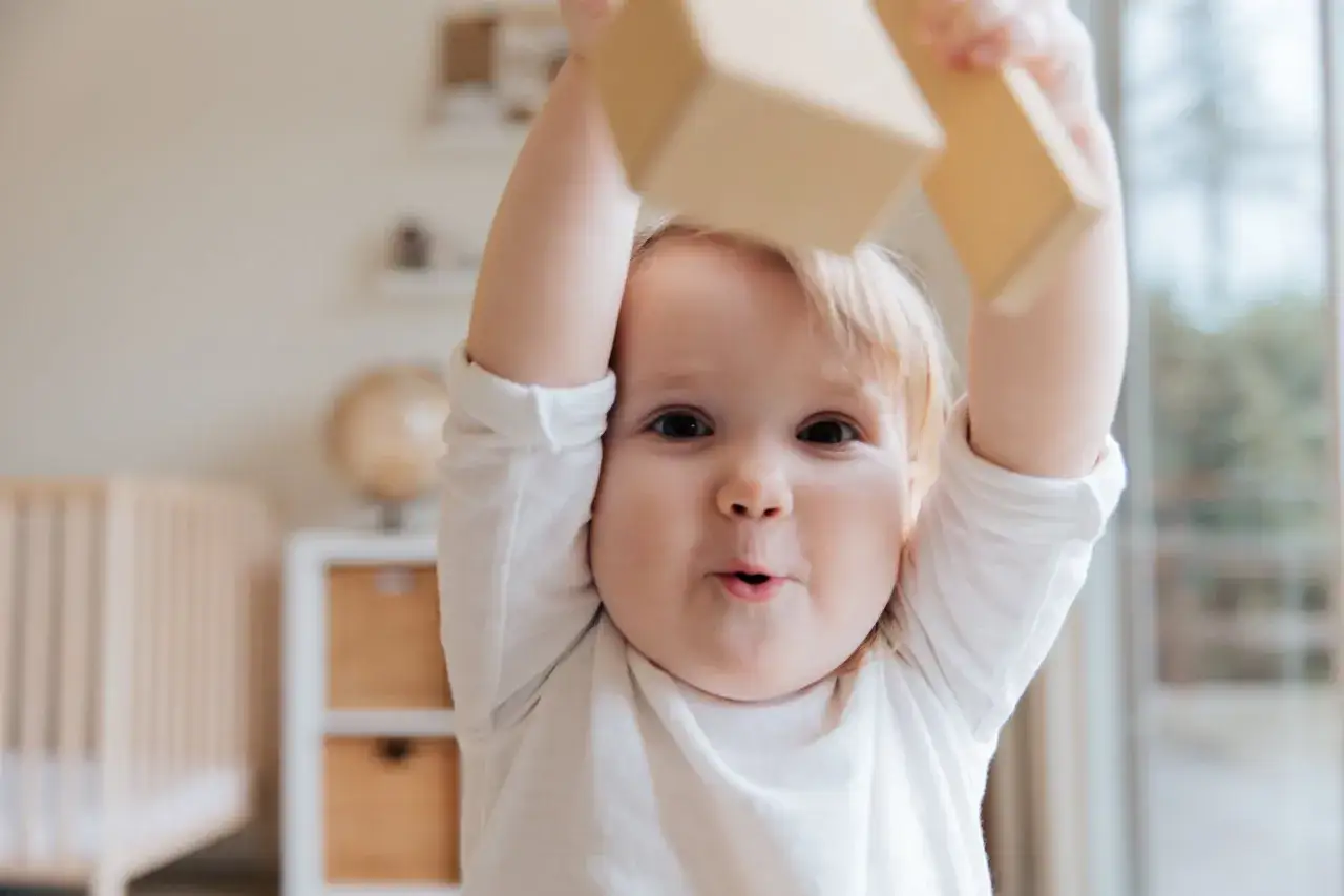 Een peuter met adhd speelt met houten blokken, met een ondeugende blik en wijd open mond.