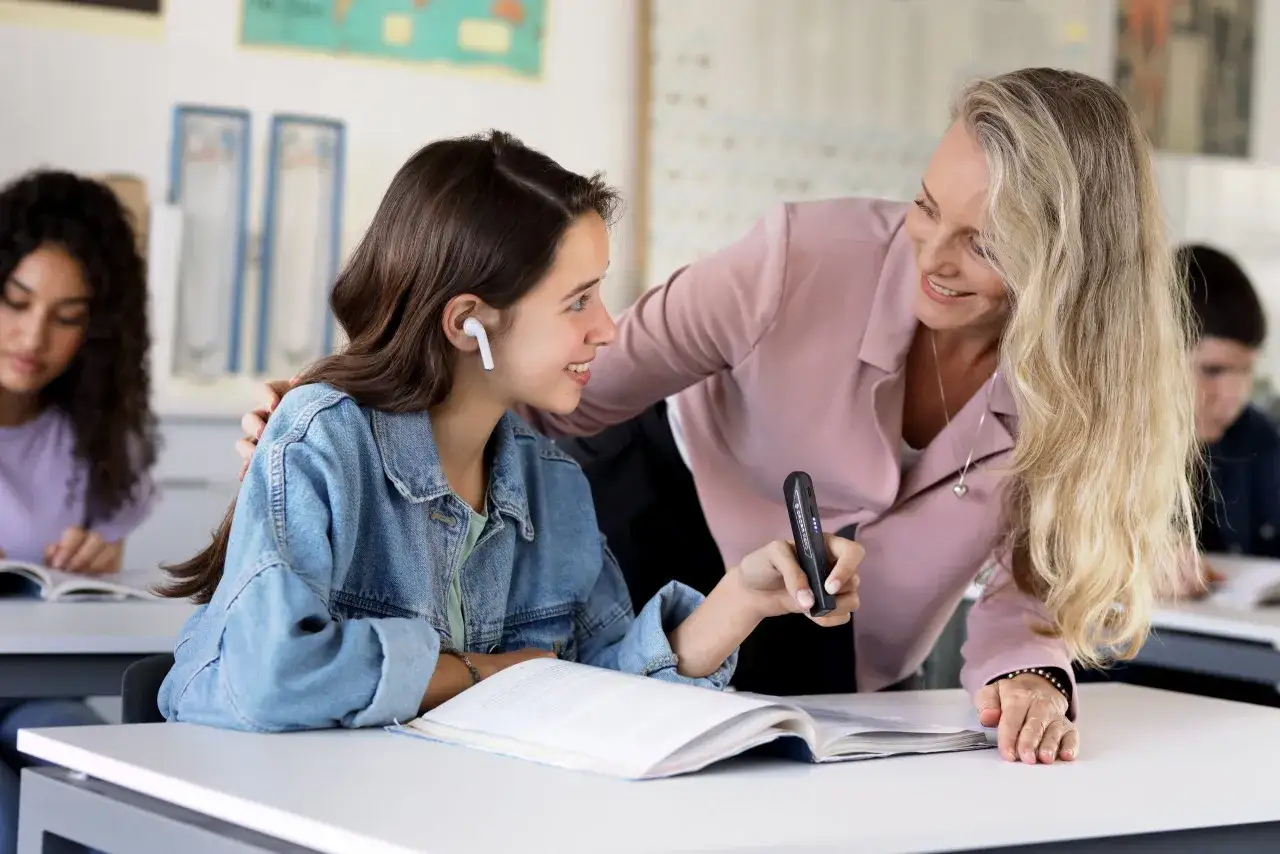 Docente helpt leerling met leesmoeilijkheden volwassenen. Ze gebruikt een scanpen om tekst voor te lezen.