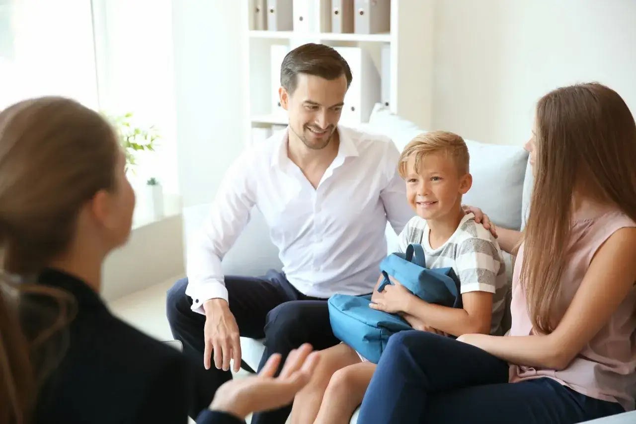 Een gezin zit op een bank, de vader legt een hand op de schouder van zijn zoon. Wat is odd? De jongen houdt een blauwe tas vast, alsof hij op reis gaat.