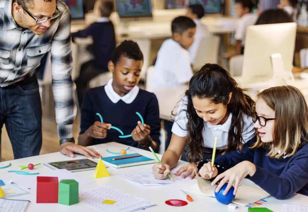 Een leraar helpt leerlingen van groep 3 die moeite hebben met lezen en rekenen. Ze gebruiken educatief materiaal om de stof beter te begrijpen.