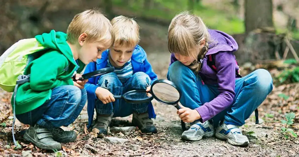 Drie kinderen van een kamp groep 8 onderzoeken de natuur met vergrootglazen.