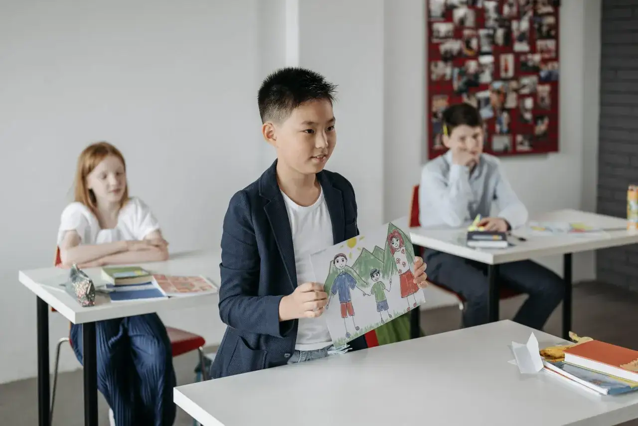 Jongen presenteert tekening van familie, een van de onderwerpen spreekbeurt. Klasgenoten luisteren aandachtig.
