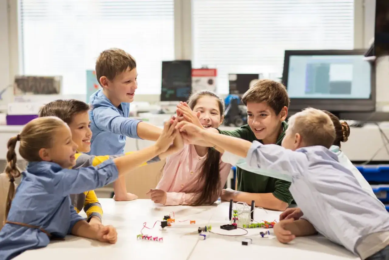 Kinderen geven elkaar een high five, een teken van sociale veiligheid op school. Ze werken samen aan een project, wat hun teamgevoel versterkt.