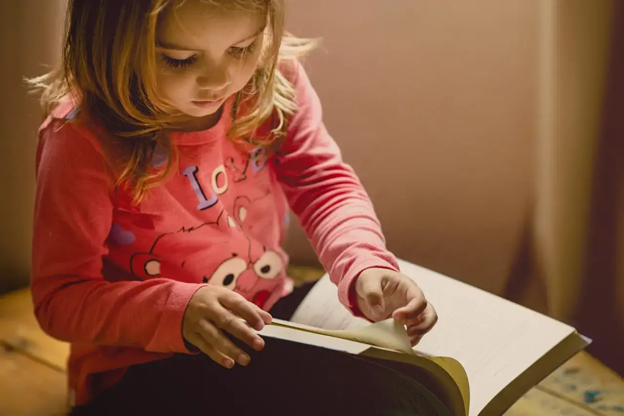 Een meisje van 6 jaar, met intense concentratie, bladert door een boek.