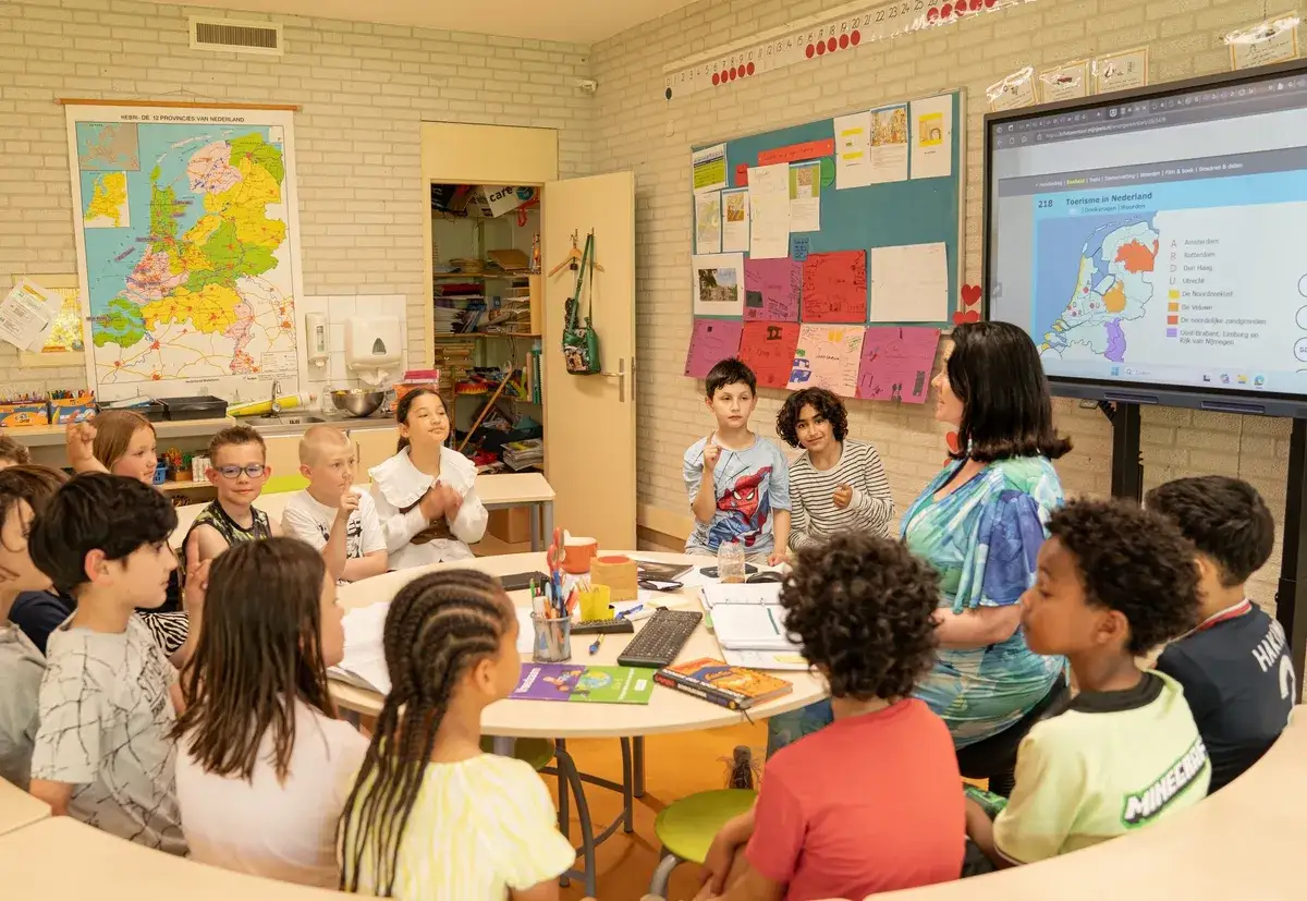 Kinderen leren actief over Nederland in een klaslokaal met een kaart en digibord. Dit is een voorbeeld van jenaplan onderwijs, waar samenwerking en ontdekking centraal staan.