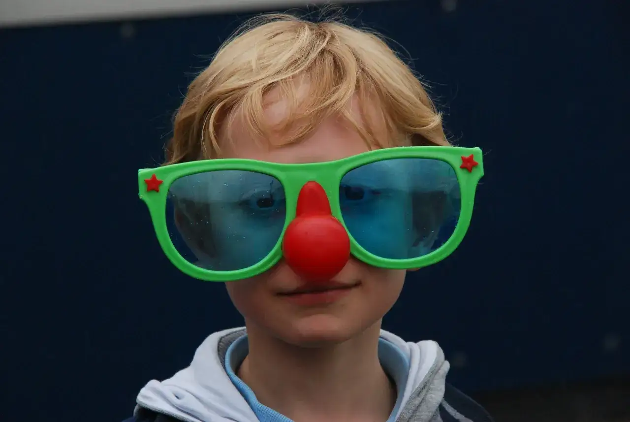 Kind met clownesk gedrag, autisme. Grote groene bril met rode neus, blauwe glazen.