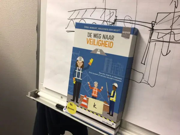 Doos van het spel "De Weg Naar Veiligheid" met bouwfiguren. Het spel moedigt aan om nog veiliger te werken, zodat iedereen veilig gespeld wordt.