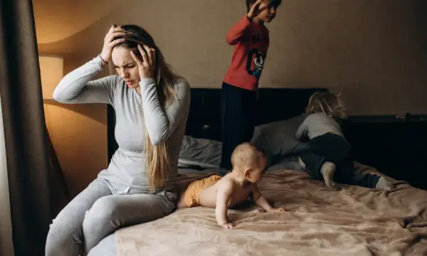 Een moeder met handen in haar hoofd, overdonderd door de drukte van haar kinderen. Een dag met adhd en autisme kan intens zijn.