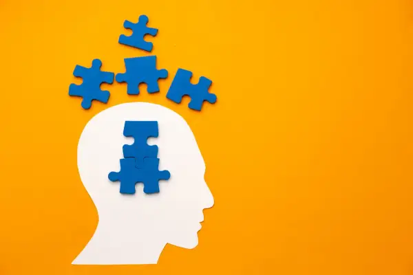 Blauwe puzzelstukjes vallen uit een witte hoofdvorm, sommigen boven, anderen in het hoofd. Het symboliseert het proces van het oplossen van gedachten, zoals bij pdd nos engels.